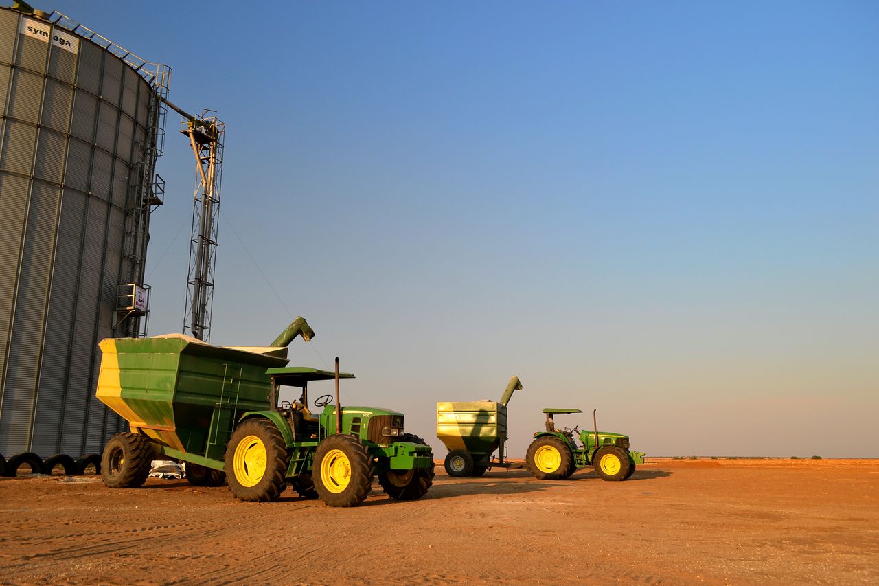 Green tractors and grain silos on a South African farm under a clear blue sky.